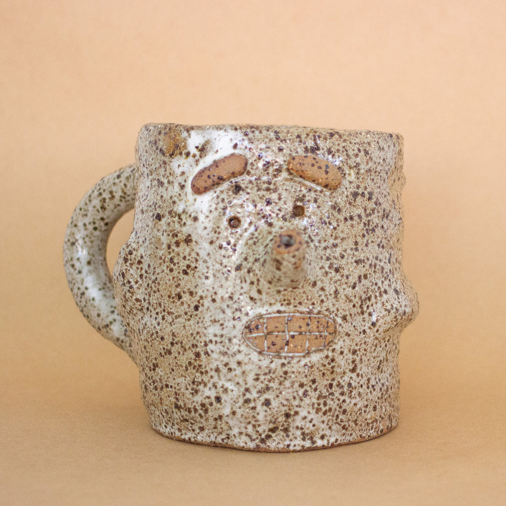 Closeup of the doink figurine. A large mug shaped sculptural piece made of stoneware clay with natural glaze. Features mouth, eyes, and nose, all hand carved into the figurine. 