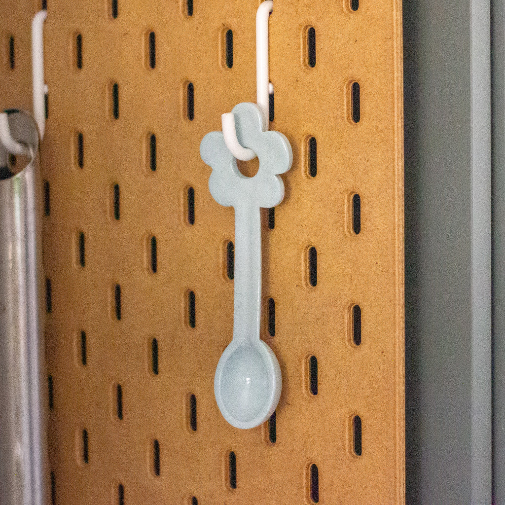 Pastel blue spoon hanging on a pegboard with a brown background