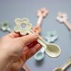 Hand holding a ceramic spoon with a flower design against a blurred background of similar spoons.