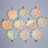 Set of ten flower-shaped ceramic plates in pastel colors on a gray background