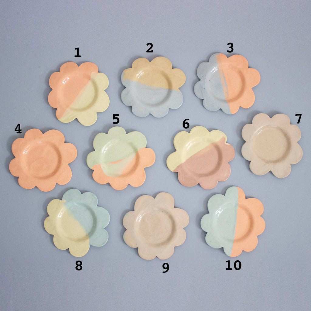 Set of ten flower-shaped ceramic plates in pastel colors on a gray background