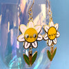Flower-shaped earrings with yellow centers and white petals on a clear stand against a blue background