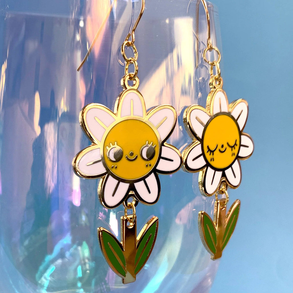 Flower-shaped earrings with yellow centers and white petals on a clear stand against a blue background
