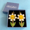 Flower-shaped earrings in a hannakin box on a light blue background