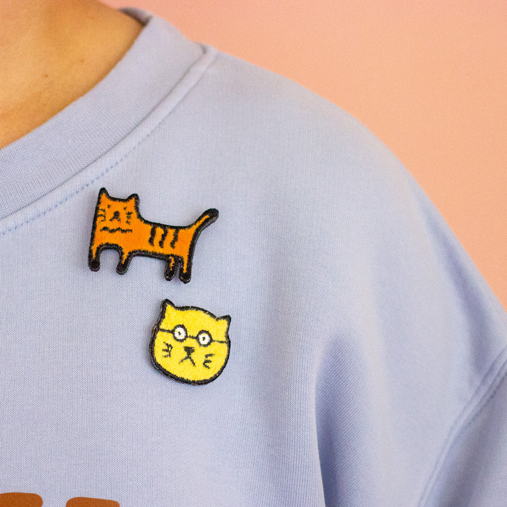 Light blue shirt with cat-themed patches on a peach background