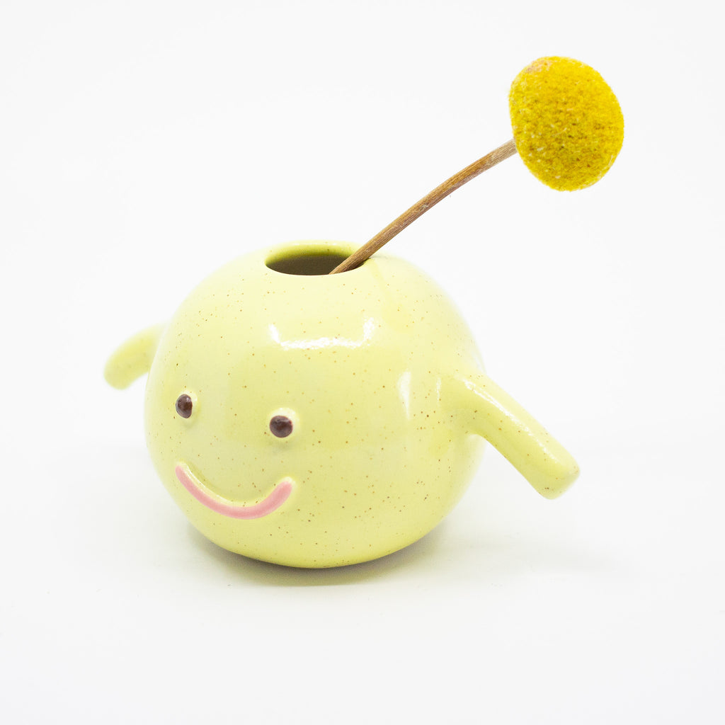 A sideview of the Esme vase holding a flower. Yellow speckled. 