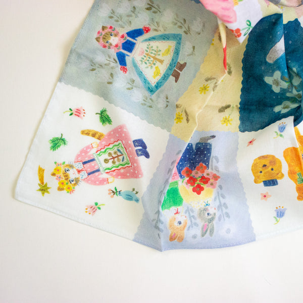 A close-up of a multicolour patchwork printed fabric featuring whimsical cartoon animal and folkloric character illustrations in pastel and bright tones, laid out on a white surface.