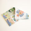 A folded cotton scarf featuring a whimsical, multi-coloured patchwork print of rabbits, flowers, and animals, displayed on a clean off-white background.
