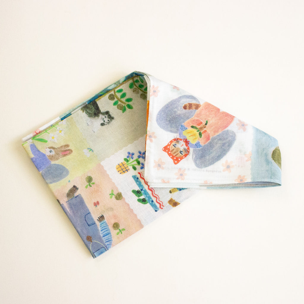 A folded cotton scarf featuring a whimsical, multi-coloured patchwork print of rabbits, flowers, and animals, displayed on a clean off-white background.