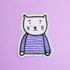 A die-cut sticker featuring a cute cat character wearing a blue and white stripe top with a holographic border, set against a plain light purple background.
