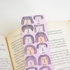 A pink bookmark with minimalist line-art illustrations of faces with long hair, placed on open book pages.