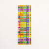 A tall, narrow rectangular bookmark featuring a dense multicolour geometric plaid pattern with intersecting vertical and horizontal stripes in yellow, orange, green, blue, purple, red, and pink on a white background.