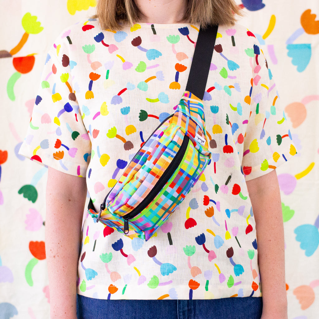 A person carrying the Farm bumbag over their shoulder. Print is multicoloured lines in a grid pattern. 