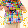 Farm easy bag used as a shoulder bag by model. Print is bright coloured lines in a grid pattern. 