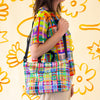 Farm easy bag used as a shoulder bag by model. Print is bright coloured lines in a grid pattern. 