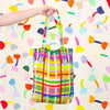 A picture of a hand holding up the farm linen tote bag. Colourful lines in a grid pattern. 