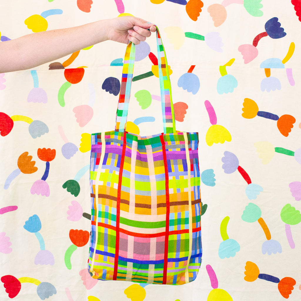 A picture of a hand holding up the farm linen tote bag. Colourful lines in a grid pattern. 