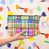 A hand holding up the farm useful bag. Multicoloured lines in grid patterns. 