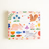 A square memo pad with a whimsical watercolour-style illustration pattern featuring a rabbit, squirrel, cat, flowers, and fish on a pale pink background, photographed against a clean white backdrop.