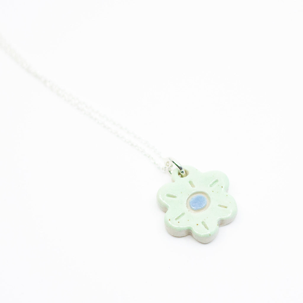 Sterling silver necklace featuring a light green ceramic flower-shaped pendant with a blue dot in the centre, displayed on a white background.