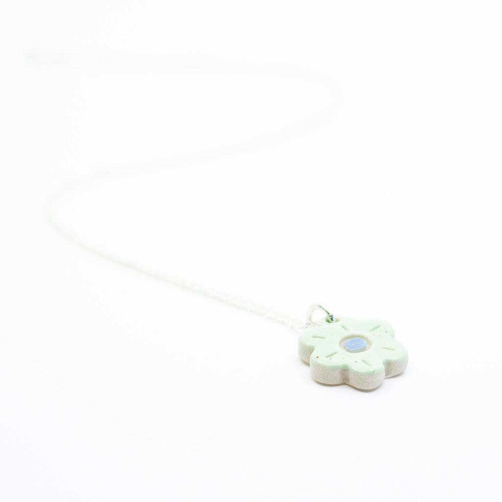 Sterling silver necklace featuring a light green ceramic flower-shaped pendant with a blue dot in the centre, displayed on a white background.