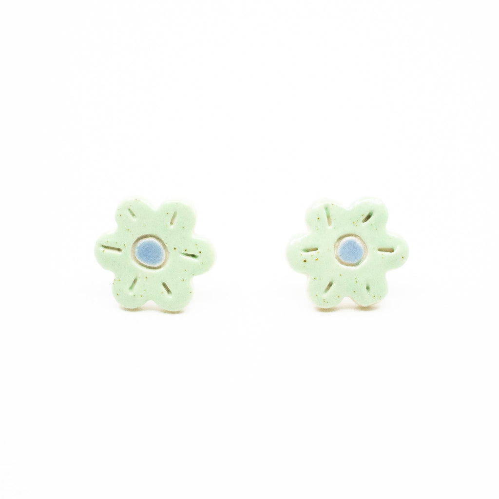 A photo of the fennel stud earrings. Ceramic earrings with a flower shape and mint green leaves with a blue centre.