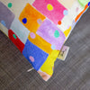 Colorful fabric cushion with geometric pattern and 'shuh' label on a textured surface