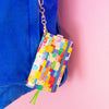 Colourful patterned notebook with keychain attached to a blue bag on a pink background