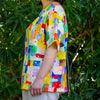 Person wearing a colourful patterned linen shirt standing in front of green foliage