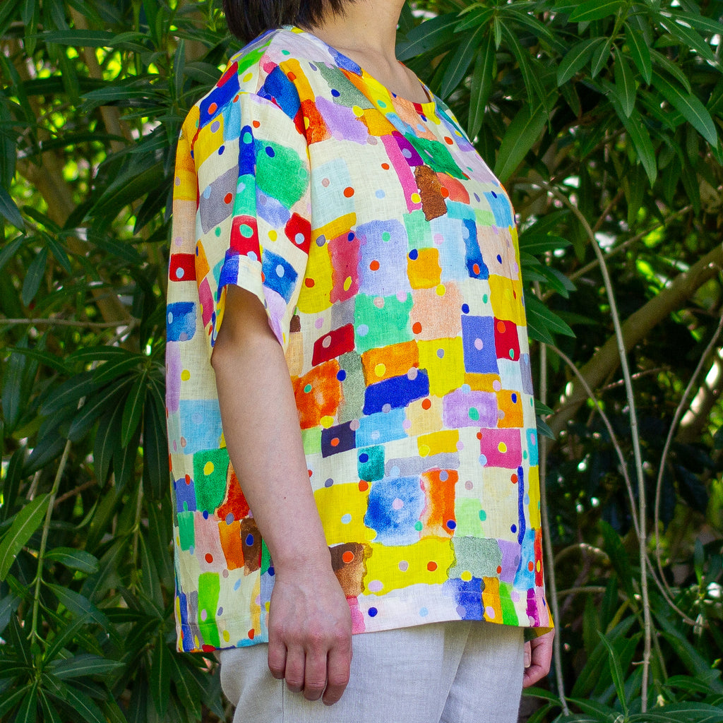 Person wearing a colourful patterned linen shirt standing in front of green foliage