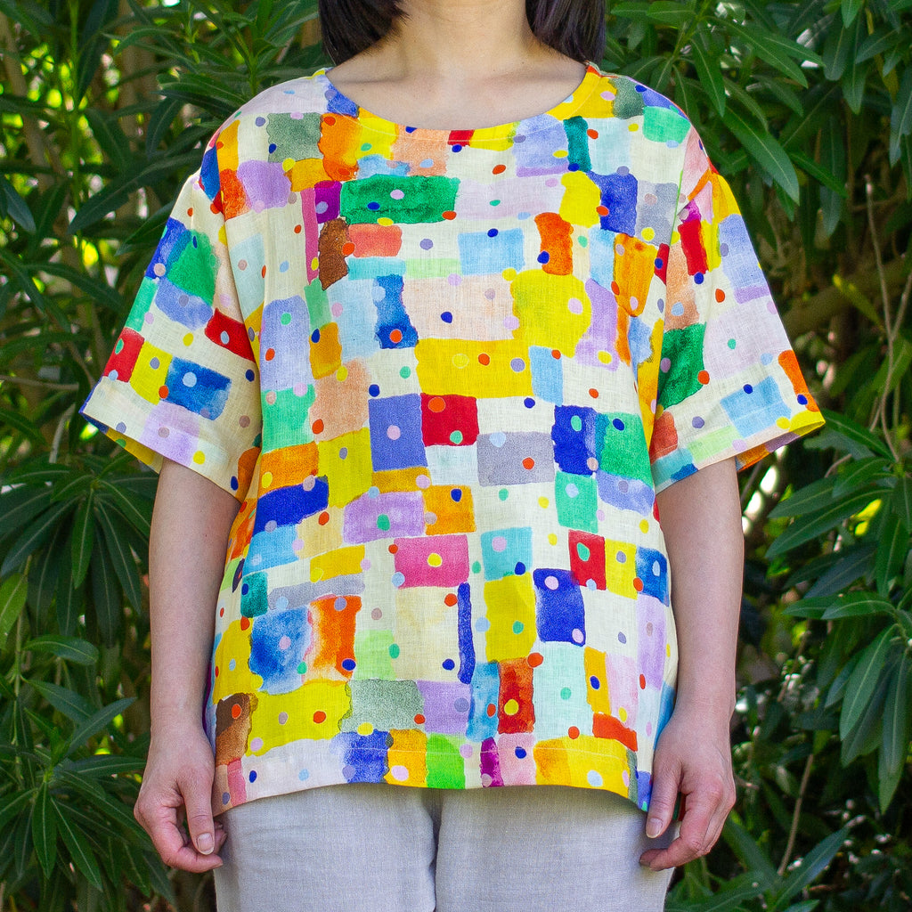 Person wearing a colourful abstract patterned linen shirt in front of green foliage