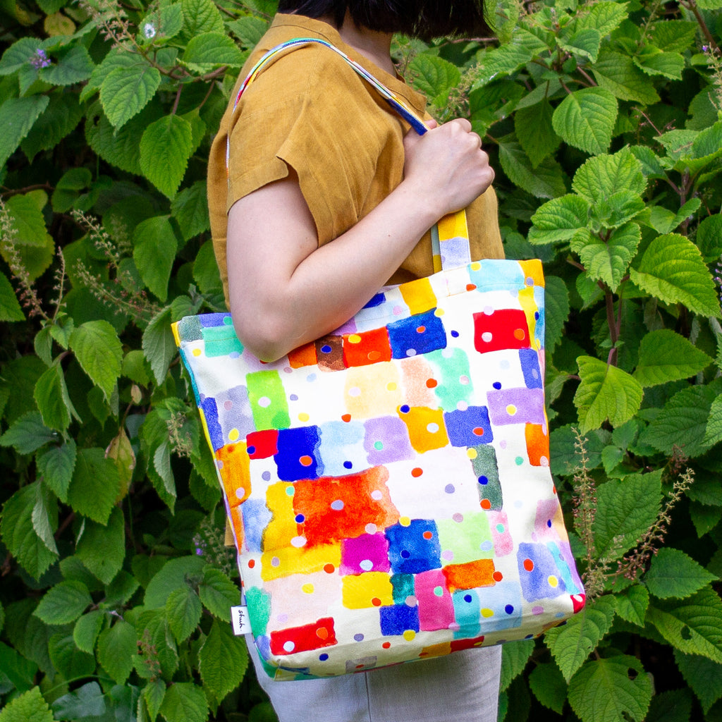 Person holding a colourful patterned bag against a green leafy background