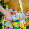 Person carrying a colourful tote bag with abstract patterns, holding it open to show the inner pocket. 