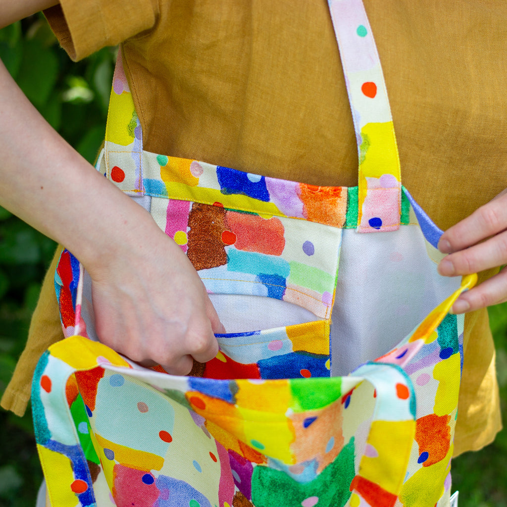Person carrying a colourful tote bag with abstract patterns, holding it open to show the inner pocket. 