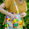 Person carrying a colourful tote bag against a green leafy background