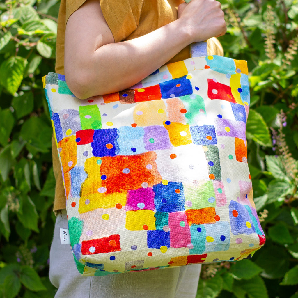 Person holding a colourful patterned tote bag against a green leafy background