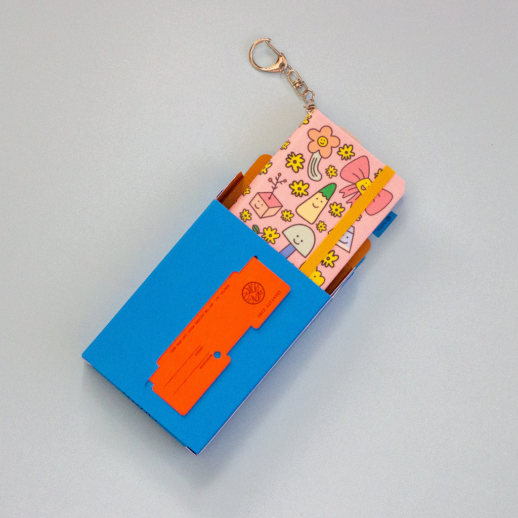A small blue box, shown on a light blue background. The box contains colourful patterned notebook, and an orange card is pulled out from the front pocket.