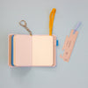A pocket notebook with a keychain ring and yellow elastic band, shown open on a light blue background next to a matching ruler.
