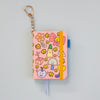 A pink mini notebook keychain with a gold keyring, decorated with cute cartoon illustrations. It features a mustard elastic closure band and a blue ribbon bookmark.