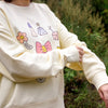 Beige sweatshirt with colourful cartoon designs against a blurred green background