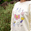 Cream sweatshirt with colourful cartoon designs worn by a person, with a natural background.
