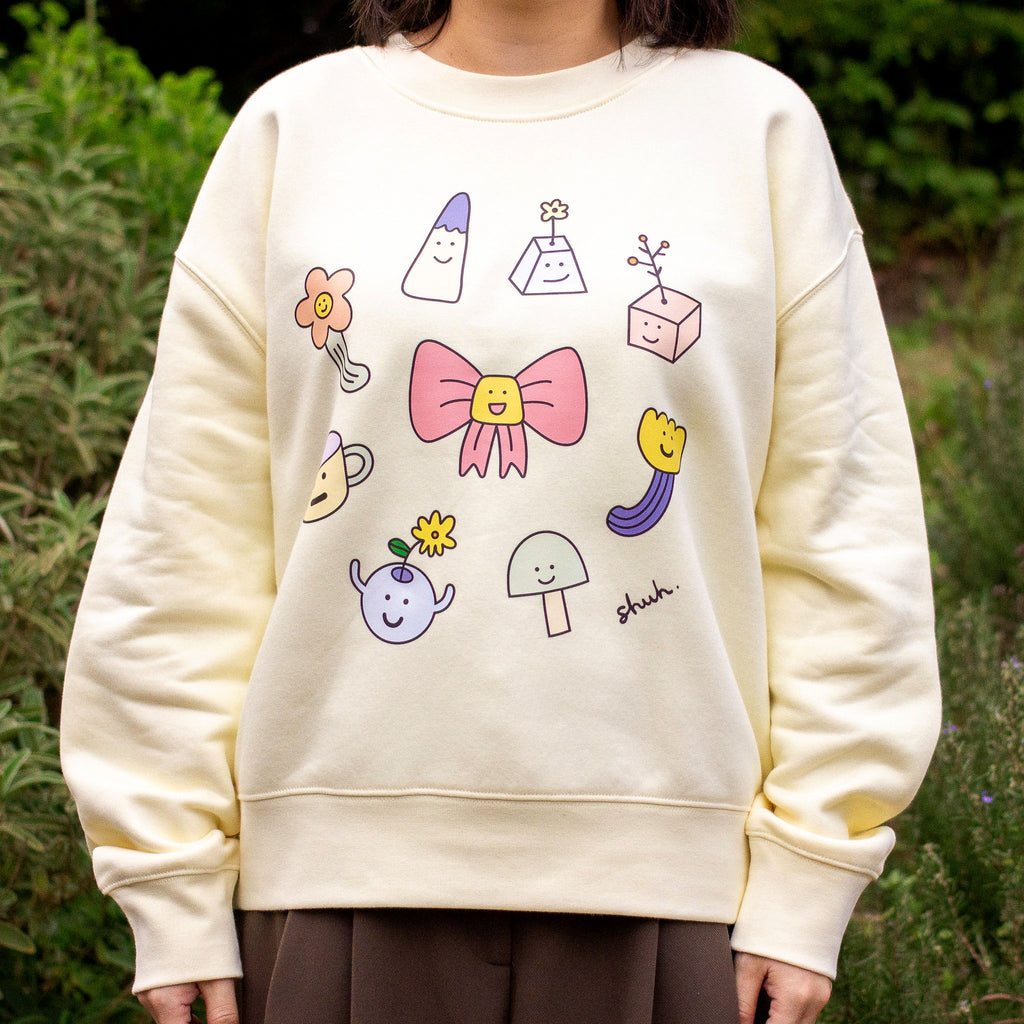 Person wearing a cream-coloured sweatshirt with colourful cartoon-like illustrations outdoors.