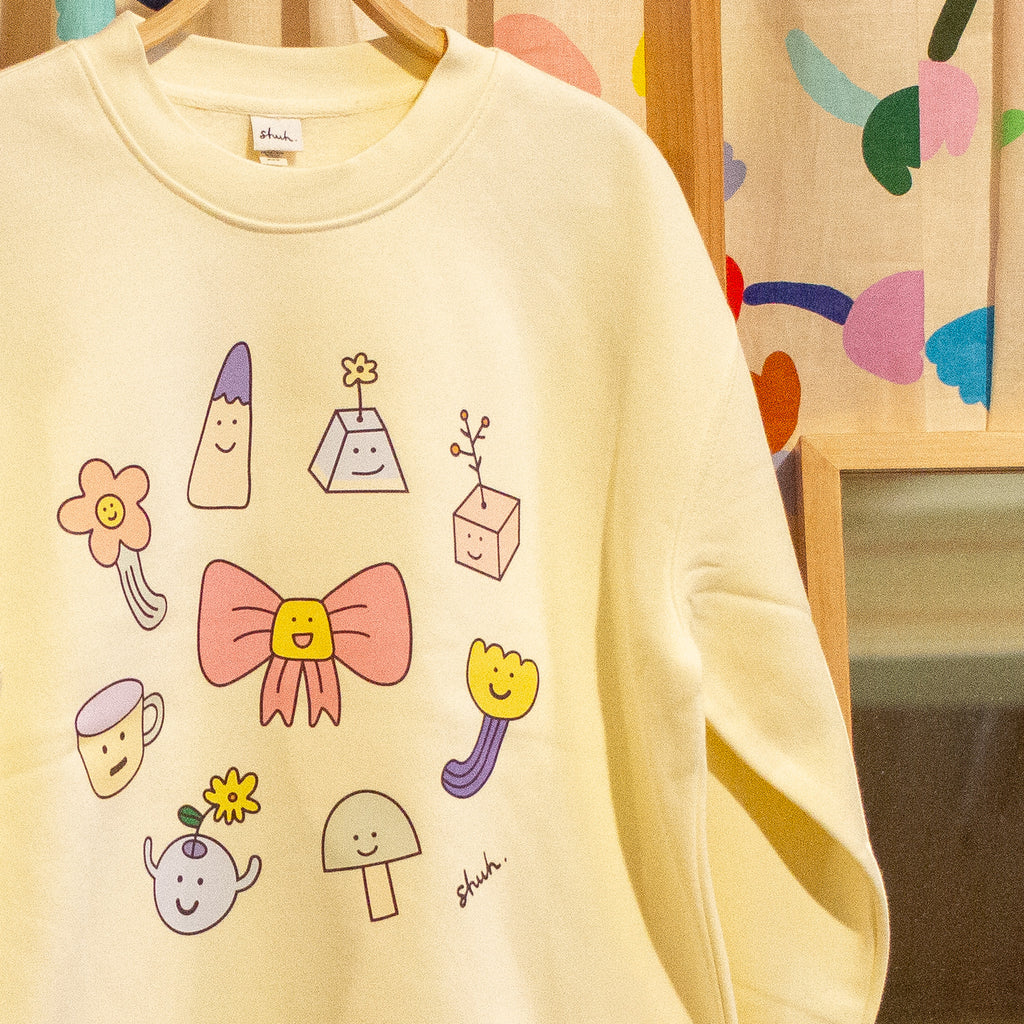 Yellow sweatshirt with colourful cartoon designs on a hanger against a patterned wall.
