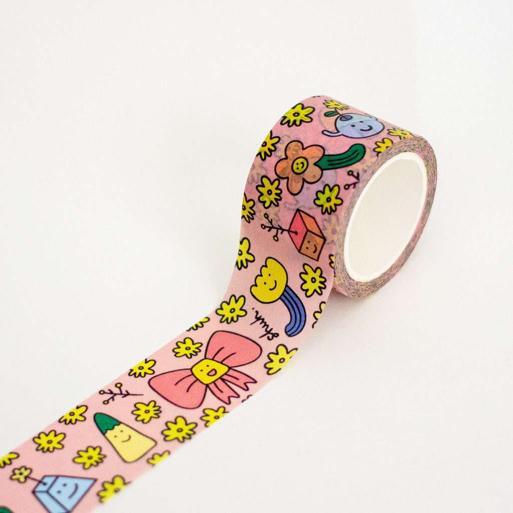 A roll of pink washi tape with a colourful cartoon pattern of flowers, bows, and smiley faces, shown partially unrolled on a white background.