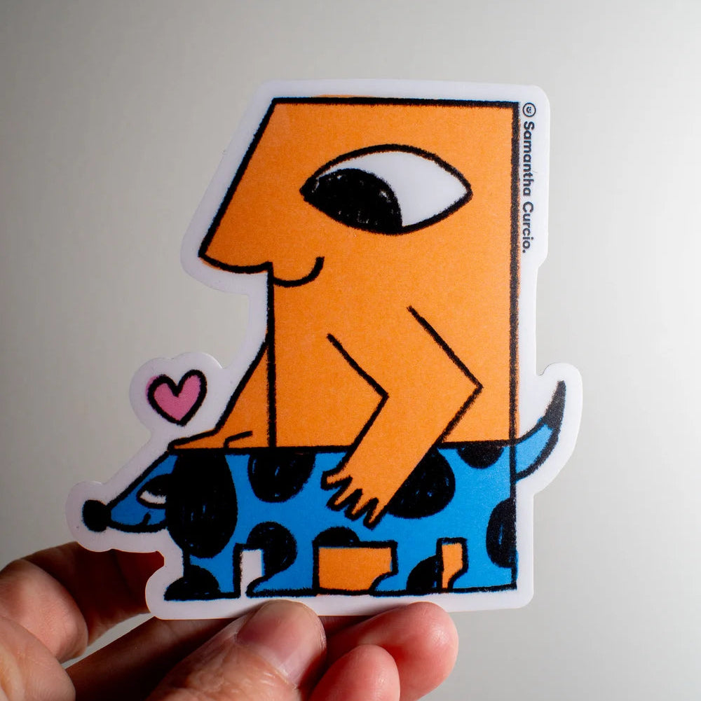 A hand holding a die-cut sticker featuring a stylised orange figure with one eye riding a blue spotted dog, with a small pink heart. The sticker has a visible artist credit reading 'Samantha Curcio' on the right edge.