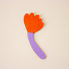 Colourful wooden wall art with an orange flower-shaped top and purple handle on a beige background