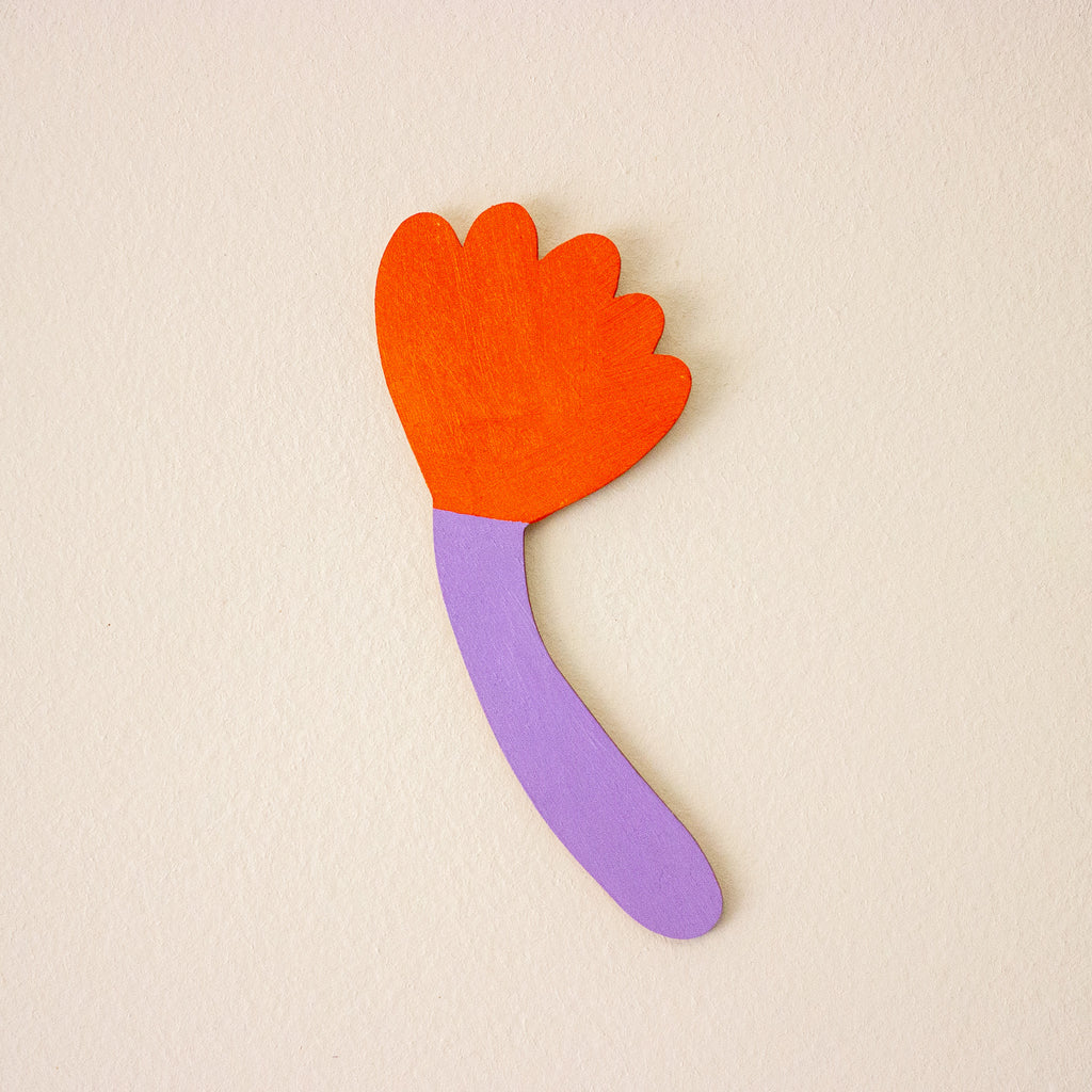 Colourful wooden wall art with an orange flower-shaped top and purple handle on a beige background
