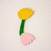 Wooden toy tulip with yellow top, green stem, and pink base on a beige background