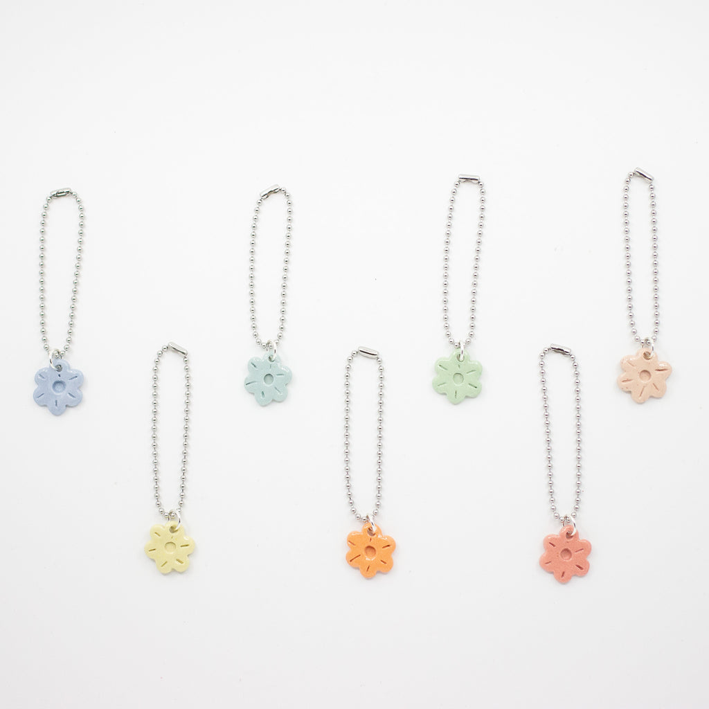 Set of six floral shaped ceramic charms on chains against a white background