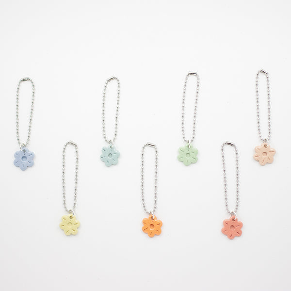 Set of six floral shaped ceramic charms on chains against a white background